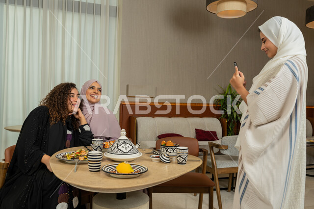 Friends meeting at a dining table in a fancy restaurant in the Emirates, having a good time with friends, taking souvenir photos via mobile, Arab Gulf Emirati friends having dinner together outside, Saudi women using mobile phones, gestures of happiness and pleasure