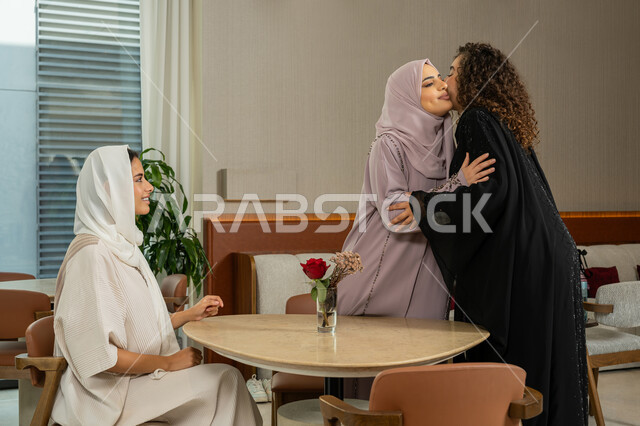 Gestures of happiness and pleasure with a gathering of friends, welcoming and greeting, a pleasant and acquainted session on a holiday, spending a pleasant time with friends, Arab Gulf Emirati female friends sitting at a table in a café, Saudi women meeting on holiday, a classy coffee shop in the Emirates, developing social relations