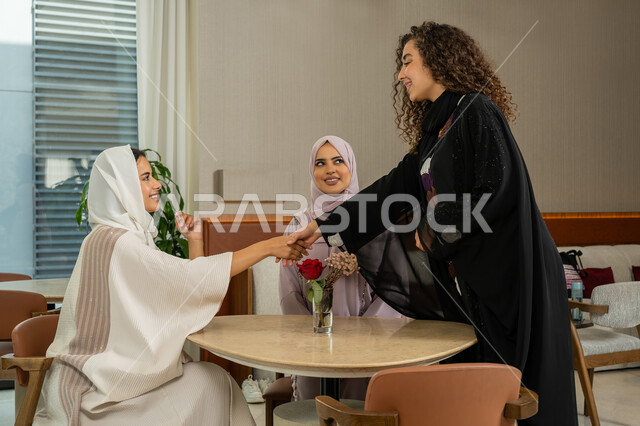 Welcoming and greeting, expressions of happiness and pleasure at a gathering of friends, a pleasant and acquainted session on a holiday, spending a pleasant time with friends, Arab Gulf Emirati female friends sitting at a table in a café, Saudi women meeting on holiday, a classy coffee shop in the Emirates, developing social relations