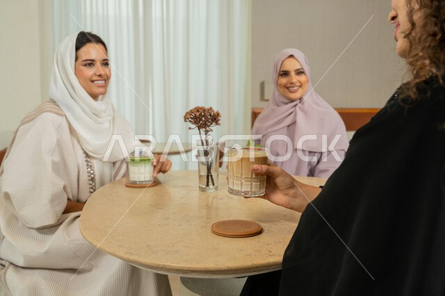 الاستمتاع بالمشروبات الباردة، ايماءات السعادة والسرور بلمة الرفاق، الدردشة والتسامر مع الأصدقاء، جلسة وناسة يوم الاجازة، كوفي شوب راقي بالامارات، تطوير العلاقات الإجتماعية، صديقات عربيات خليجيات اماراتيات يجلسن على طاولة في المقهى، نساء سعوديات يتبادلون الحديث