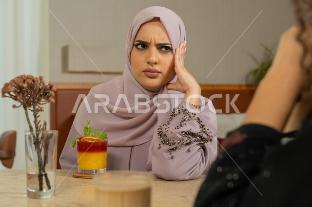 ايماءات الاستغراب والاستفهام، جلسة وناسة وتعارف في يوم العطلة، التسامر والدردشة وقضاء وقت مع الأصدقاء، كوفي شوب راقي بالامارات، تطوير العلاقات الإجتماعية، امرأة عربية خليجية اماراتية محجبة تجلس مع رفاقها على طاولة في المقهى، نساء سعوديات يتبادلون الحديث