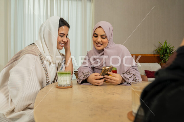 قضاء وقت ممتع مع الأصدقاء، جلسة وناسة وتعارف يوم الاجازة، كوفي شوب راقي بالامارات، متابعة مواقع التواصل الاجتماعي عبر الهاتف المحمول، تطوير العلاقات الإجتماعية، صديقات عربيات خليجيات اماراتيات يجلسن على طاولة في المقهى، نساء سعوديات يقومون بتصفح الانترنت