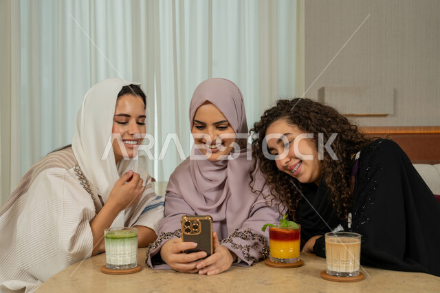 متابعة مواقع التواصل الاجتماعي عبر الهاتف المحمول، تطوير العلاقات الإجتماعية، قضاء وقت ممتع مع الأصدقاء، جلسة وناسة وتعارف يوم الاجازة، صديقات عربيات خليجيات اماراتيات يجلسن على طاولة في المقهى، نساء سعوديات يقومون بتصفح الانترنت، كوفي شوب راقي بالامارات