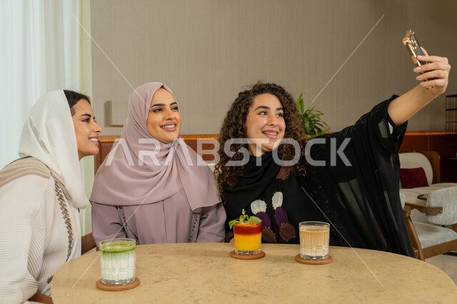 الاستمتاع بقضاء الوقت مع الأصدقاء، جلسة وناسة وتعارف يوم الاجازة، التقاط صور السيلفي التذكارية، تطوير العلاقات الإجتماعية، صديقات عربيات خليجيات اماراتيات يجلسن على طاولة في المقهى، نساء سعوديات يلتقطون صورة الشخصية عبر الهاتف المحمول، كوفي شوب راقي بالامارات