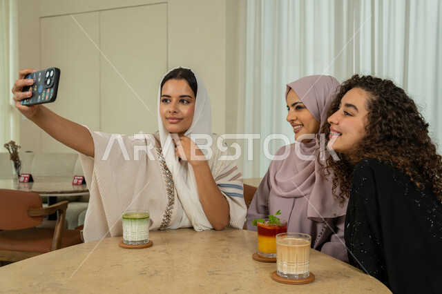 جلسة وناسة وتعارف يوم الاجازة، قضاء وقت ممتع برفقة الأصدقاء، التقاط صور السيلفي التذكارية، تطوير العلاقات الإجتماعية، صديقات عربيات خليجيات اماراتيات يجلسن على طاولة في المقهى، نساء سعوديات يلتقطون صورة الشخصية عبر الهاتف المحمول، كوفي شوب راقي بالامارات