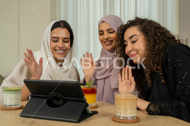الاستمتاع بمشروب بارد في كوفي شوب، تطوير العلاقات الإجتماعية، قضاء وقت ممتع مع الأصدقاء، تصفح الإنترنت من جهاز التابلت، القاء التحية والسلام، صديقات عربيات خليجيات اماراتيات يجلسن على طاولة في المقهى، نساء سعوديات يقومون ببث مباشر عبر مواقع التواصل الاجتماعي