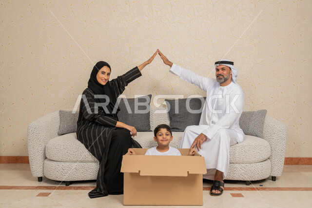 الترابط الأسري والوحدة العائلية، تعابير السعادة لامتلاك سكن جديد، تنظيم وترتيب المنزل، نقل صناديق الأغراض المنزلية، عائلة عربية خليجية اماراتية يجلسون على اريكة في البيت الجديد وبجانبهم حاويات كرتونية، مفهوم الاسكان والتمليك والاستقرار العائلي