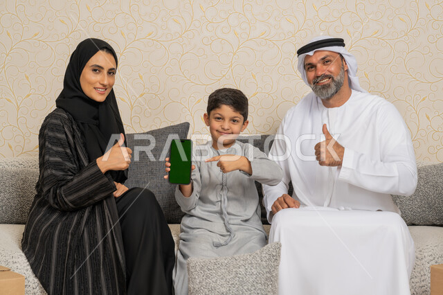 عرض شاشة خضراء فارغة كروما،  ولد اماراتي يشير باصبع السبابة الى الهاتف المحمول، زوجان عربيان خليجيان اماراتيان يرفعان اصبع الابهام بايماءات الجودة ، تعابير القبول والرضا، عائلة عربية خليجية اماراتية يجلسون على اريكة في البيت الجديد وبجانبهم حاويات كرتونية