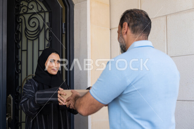 طلب المنتجات والتسوق عبر الإنترنت, خدمة الشحن ذات الجودة العالية، شبكة التوصيل الاونلاين في الخليج، سيدة سعودية تقوم بإستلام البضائع بالوقت المحدد و بشكل سليم، صورة مقربة لامرأة عربية خليجية اماراتية تأخذ صناديق كرتونية من مندوب عربي خليجي اماراتي يرتدي الزي الكاجوال