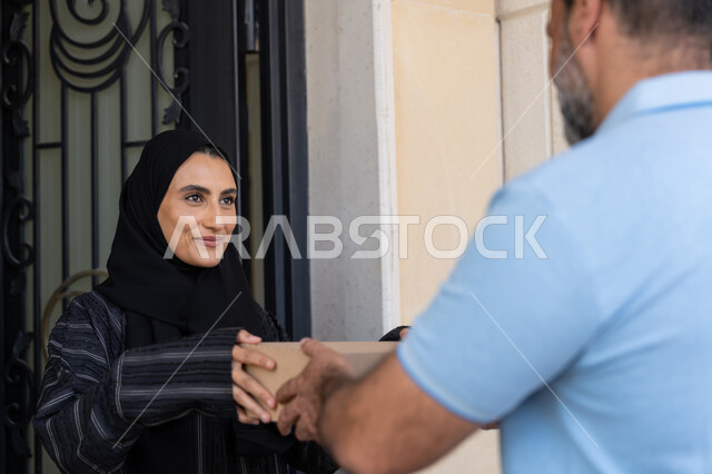 Shopping and ordering products online, high quality shipping service, online delivery network in the Gulf, Saudi woman receiving goods on time and in good condition, close-up of an Arab Gulf Emirati woman taking cardboard boxes from an Arab Gulf Emirati representative wearing casual clothes