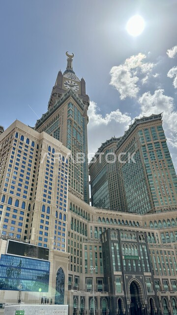 العبادة والتقرب إلى الله، مبنى برج الساعة الملكي في مكة المكرمة، الفن الهندسي المعماري لناطحات السحاب، معلم ديني إسلامي مقدس، بيت الله الحرام في الحرم المكي الشريف في المملكة العربية السعودية، منظر الغيوم في السماء في النهار