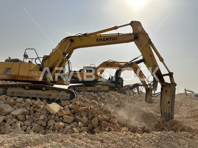 جرافات ضخمة تعمل في الحفر ورفع الأنقاض والأتربة في موقع العمل، وظيفة ومهنة هندسية صناعية في السعودية، تحسين البنية التحتية لإقامة المباني والمشاريع الحديثة في مدينة الرياض، مفهوم الهندسة المعمارية والإنشاء، الاعتماد على الآلات والمعدات الثقيلة في أعمال البناء