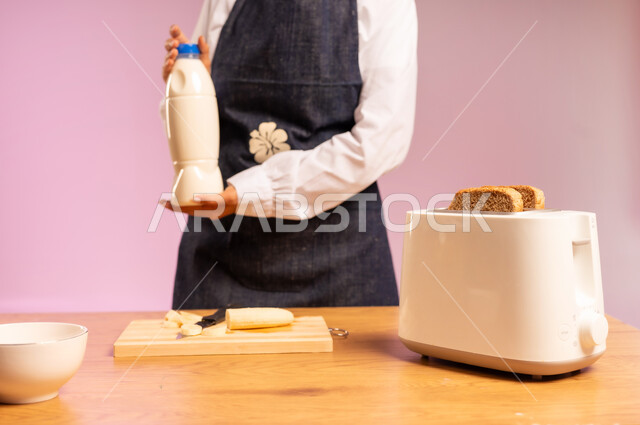 اتباع نظام غذائي، وجبة طعام صحية، تحضير رقائق الذرة في طبق أبيض، مفهوم الأكل الصحي، بورتريه مقرب لامرأة عربية خليجية سعودية ترتدي اليونفر تقوم بحمل علبة الحليب و اعداد الفطور الصباحي على طاولة المطبخ، خلفية ملونة