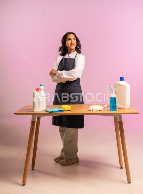 المهام والأعمال المنزلية الروتينية، التطهير والتنظيف في المنازل,  بورتريه لمرأة عربية خليجية سعودية ترتدي اليونفور وتحمل بيدها مواد ومستلزمات التعقيم، أداء مهام المطبخ، الجسم بالطول الكامل، خلفية ملونة