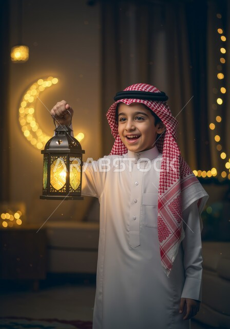 تحف وزينة الاحتفالات في السعودية، الاستعداد لقدوم شهر رمضان, المناسبات الدينية والأعياد الإسلامية,  طفل عربي خليجي سعودي مبتسم يرتدي الثوب التقليدي والشماغ ويحمل الفانوس, هلال رمضاني مضيئ