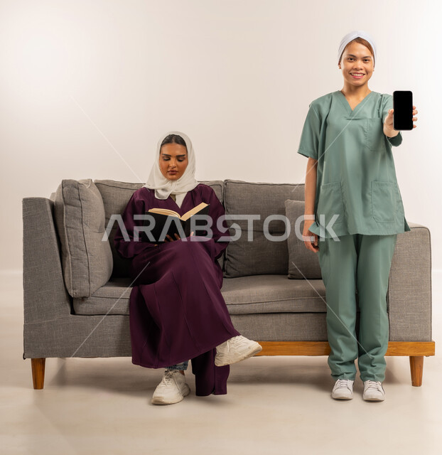 منصة وتطبيق لاستقدام العماله المنزليه المدربة، الخدمات الإلكترونيه المتقدمه لتوفير العاملات المرخصة والمؤهله، بورتريه لسيدة عربية خليجية اماراتية محجبة ترتدي عباءة خمرية تجلس على الاريكة وتقوم بقراءة كتاب وعاملة نظافة فلبينية تحمل بيدها هاتف بشاشة سوداء فارغة ، خلفية بيضاء