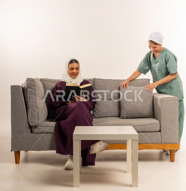 المهام والأعمال المنزلية الروتينية، توجيه وإشراف مدبرة المنزل على خدمة التنظيف، عاملة نظافة تقوم بترتيب الوسائد، بورتريه لسيدة عربية خليجية سعودية محجبة ترتدي عباءة خمرية تجلس على الأريكة تقوم بقراءة الكتب و تستعين بخادمة أجنبية داخل المنزل، خلفية بيضاء