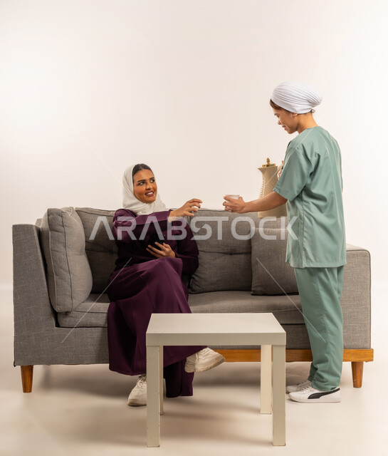 استقدام العماله المنزليه المرخصه والمؤهله، الاستعانة بمساعدة عاملة فلبينية في المنزل، حسن الضيافة والاستقبال، أداء الأعمال المنزلية الروتينية على أكمل وجه، بورتريه لسيدة عربية خليجية سعودية محجبة ترتدي عباءة خمرية تجلس على الأريكة وتأخد كوب القهوة من الخادمة، خلفية بيضاء