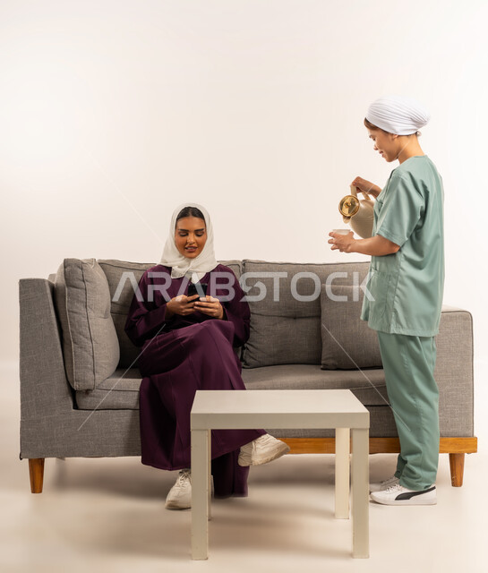 Hiring licensed and qualified domestic workers, hiring a Filipino domestic worker, hospitality and reception, performing routine household chores to the fullest, portrait of a veiled Saudi Arabian Gulf woman wearing a burgundy abaya sitting on the couch and taking a cup of coffee from the maid, white background