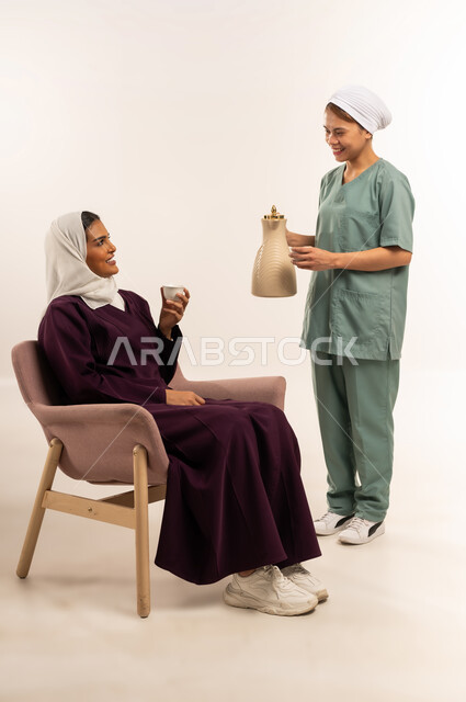 حسن الضيافة والاستقبال، أداء الأعمال المنزلية الروتينية على أكمل وجه، بورتريه لسيدة عربية خليجية سعودية محجبة ترتدي عباءة خمرية تجلس على الأريكة وتأخد كوب القهوة من الخادمة، الاستعانة بمساعدة عاملة فلبينية في المنزل، استئجار العماله المنزليه المرخصه والمؤهله، خلفية بيضاء