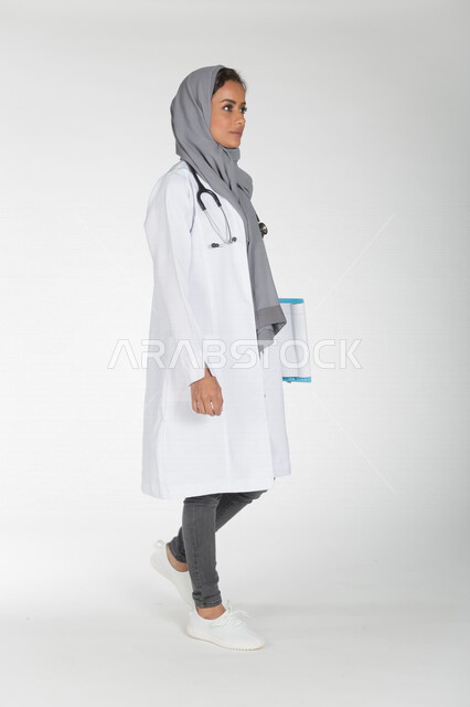 بورتريه لطبيبة عربية خليجية سعودية تمسك بيدها دفتر الملاحظات وتمشي مسرعة، مفهوم الطب والرعاية الصحية، ايماءات وجه ويدين مختلفة، تقديم الخدمات الصحية، صورة بطول الجسم الكامل، خلفية بيضاء