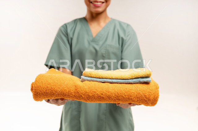 استقدام العمالة الاجنبية المدربة والمؤهلة، جودة الخدمات في السعودية، الأعمال والمهام المنزلية الروتينية، وظائف ومهن نسائية، بورتريه مقرب لعاملة نظافة فلبينية ترتدي اليونيفورم الخاص بالعمل وتحمل بيدها المناشف النظيفة، خلفية بيضاء