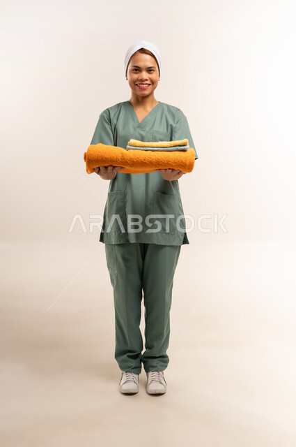 Routine household chores and tasks, women's jobs and professions, recruitment of trained and qualified foreign workers, portrait of a Filipino cleaning lady wearing a work uniform and holding clean towels in her hand, full body length, white background