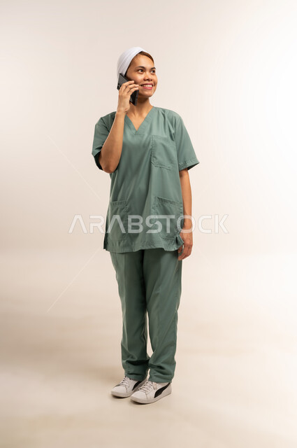 الخدمات الإلكترونيه المتقدمه لتوفير العاملات  والخادمات المؤهله، استقدام العمالة الاجنبية المدربة والمؤهلة، بورتريه لعاملة نظافة فلبينية ترتدي اليونيفورم الخاص بالعمل تقوم بإجراء مكالمة صوتية عبر الهاتف المحمول، مهن ووظائف نسائية، الطول الكامل للجسم، خلفية بيضاء