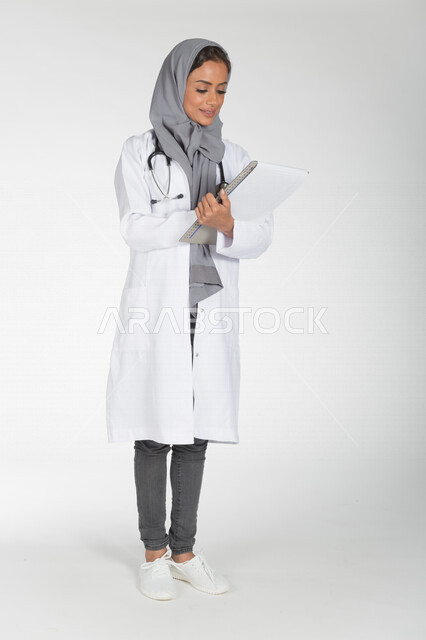 بورتريه لطبيبة عربية خليجية سعودية تقوم بكتابة وتدوين الملاحظات، مفهوم الطب والرعاية الصحية، ايماءات وجه ويدين مختلفة، تقديم الخدمات الصحية، صورة بطول الجسم الكامل، خلفية بيضاء
