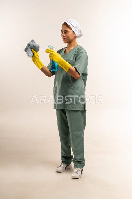 الأعمال والمهام المنزلية الروتينية، جودة الخدمات في السعودية، وظائف ومهن نسائية، استقدام العمالة الاجنبية المدربة والمؤهلة، بورتريه لعاملة نظافة فلبينية ترتدي اليونيفورم الخاص بالعمل والقفازات تحمل أدوات التنظيف، الطول الكامل للجسم، خلفية بيضاء