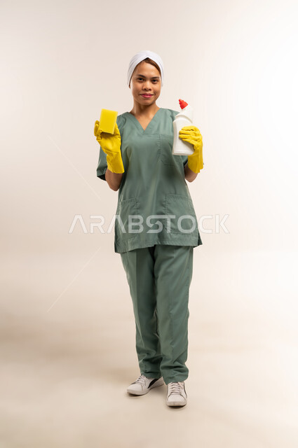 المهام والأعمال المنزلية الروتينية، جودة الخدمات في السعودية، وظائف ومهن نسائية، استقدام العمالة الاجنبية المدربة والمؤهلة، بورتريه لعاملة نظافة فلبينية ترتدي اليونيفورم الخاص بالعمل والقفازات تنظر للكاميرا وتحمل أدوات التنظيف، الطول الكامل للجسم، خلفية بيضاء