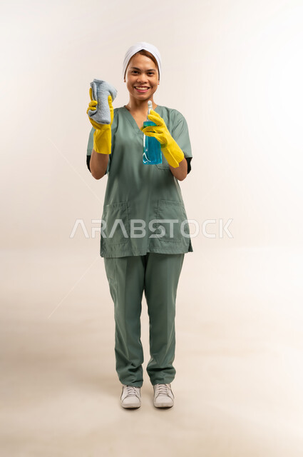 الأعمال والمهام المنزلية الروتينية، جودة الخدمات في السعودية، وظائف ومهن نسائية، استقدام العمالة الاجنبية المدربة والمؤهلة، بورتريه لعاملة نظافة فلبينية ترتدي اليونيفورم الخاص بالعمل والقفازات تنظر للكاميرا وتحمل أدوات التنظيف، الطول الكامل للجسم، خلفية بيضاء