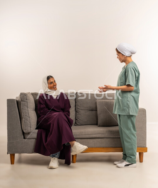 استقدام العماله المنزليه المرخصه والمؤهله، توفير خدمات العناية بالمنزل، الإحسان في التعامل مع الخادمات في البيوت، بورتريه لامرأة عربية خليجية سعودية محجبة ترتدي عباءة خمرية تجلس على اريكة تتحدث مع العاملة الفلبينية، مدبرة منزل تستعين بخادمة أجنبية، خلفية بيضاء