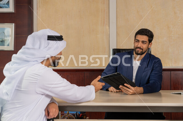 مناقشة مهام العمل باستخدام التابليت، مفهوم الإدارة المتعاونة، الوحدة والعمل الجماعي لتطوير العمل وحل المشكلات، تحقيق اهداف الشركة، مكاتب و شركات خليجية، رجل اعمال يرتدي البدلة الرسمية يجلس في المكتب مع زميله, مهنة ووظيفة اماراتية