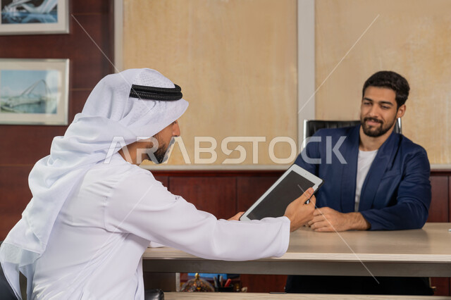 مفهوم الإدارة المتعاونة، الوحدة والعمل الجماعي لتطوير العمل وحل المشكلات، مناقشة مهام العمل باستخدام التابليت، تحقيق اهداف الشركة، مكاتب و شركات خليجية، رجل اعمال يرتدي البدلة الرسمية يجلس في المكتب مع زميله, مهنة ووظيفة اماراتية