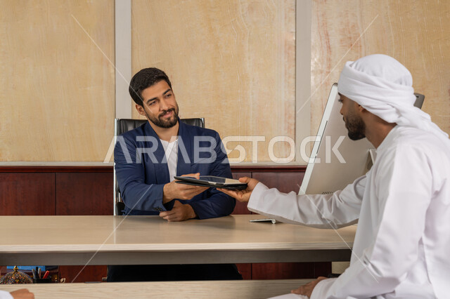 تحقيق اهداف الشركة، مناقشة مهام العمل باستخدام التابليت، مكاتب و شركات خليجية، الوحدة والعمل الجماعي لتطوير العمل وحل المشكلات، رجل اعمال يرتدي البدلة الرسمية يجلس في المكتب مع زميله, مفهوم الإدارة المتعاونة، مهنة ووظيفة اماراتية
