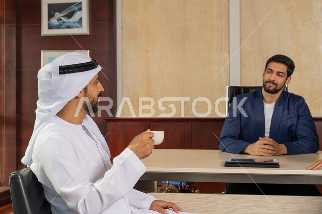 شرح خطط و استراتيجيات العمل, التعارف والصداقات وبناء العلاقات الاجتماعية, بيئة مريحة في الشركات الاماراتية, رجل أعمال عربي يرتدي البدلة الرسمية يجلس في المكتب داخل مقر الشركة مع زميله، الاستمتاع باحتساء القهوة