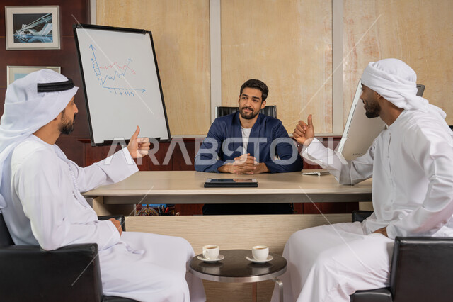 بناء العلاقات الاجتماعية, مهنة ووظيفة اماراتية, رجلان عربيان خليجيان سعوديان يرتديان الكندورة يقومان بالاتفاق على انجاز المهام يرفعان اصابع الابهام بعلامة الجودة و الرضا, رجل أعمال عربي مبتسم يرتدي الزي الرسمي يجلس في المكتب داخل مقر الشركة