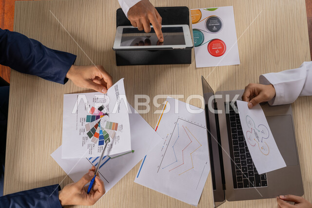 Using advanced modern technology, reviewing the annual report, studying and discussing the progress of the business strategy, pictures from above of businessmen sitting in the office inside the company headquarters, agreeing on the business project, unity and teamwork to develop the business and solve problems, an Emirati profession and job