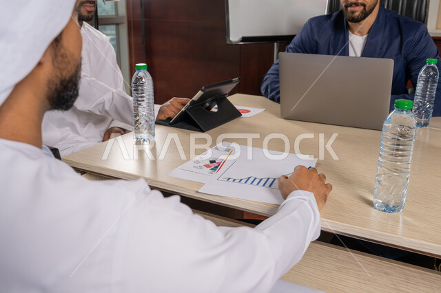 دراسة ومناقشة سير استراتيجية العمل، استخدام التقنية الحديثة المتطورة، صور مقربة لرجلان عربيان اماراتيان خليجيان يرتديان الكندورة مع رجل بالبدلة الرسمية يجلسون في المكتب داخل مقر الشركة, الاتفاق على المشروع التجاري، مراجعة التقرير السنوي، مهنة ووظيفة اماراتية