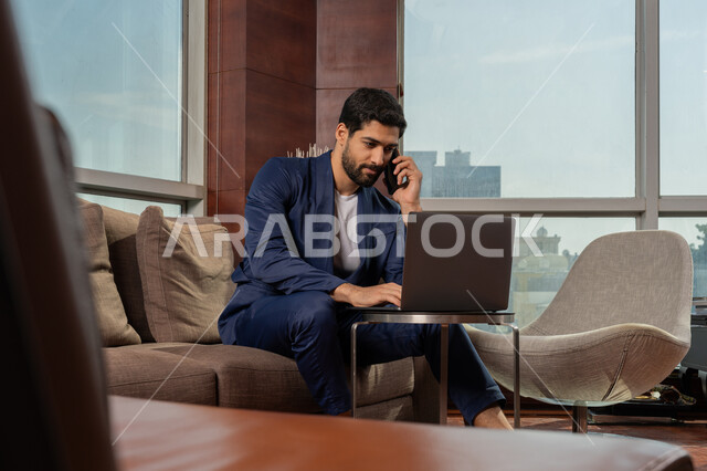 جلسه عمل عن بعد, اجراء مكالمة هاتفية عبر الجوال, أداء المهام اليومية داخل مقر الشركه، رجل أعمال عربي خليجي اماراتي يرتدي الزي الرسمي يقوم بالعمل على جهاز الحاسوب المحمول، دراسه المشاريع ومراجعه التقارير السنويه، استخدام التقنية الحديثة المتطورة