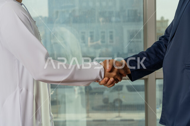 Expanding business areas, partnership in business and projects, friendships and acquaintances and building social relationships, concluding new successful business deals, a close-up of the hand of an Arab Gulf Emirati gentleman wearing a kandura shaking hands with a businessman inside the company headquarters