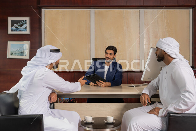 Gulf offices and companies, unity and teamwork to develop work and solve problems, a group of Arab Gulf Emirati businessmen sitting in the office, discussing work tasks using a tablet, achieving company goals, Emirati profession and job