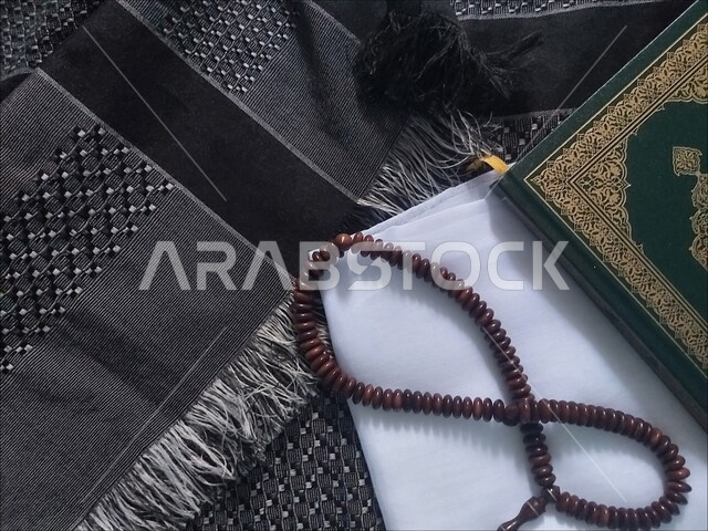 مفهوم الإجتهاد في العباده و الدعاء وطلب المغفرة في شهر رمضان المبارك، تلاوة القران و حفظ و تفسير كلام الله, صورة علوية عامودية للمصحف الشريف مع سبحة مصنوعة من الخرز للتسبيح والذكر على سجادة الصلاة