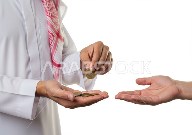 مفهوم التكافل الاجتماعي ومساعدة المحتاجين، العبادة والتقرب الى الله، بورتريه مقرب ليد رجل عربي خليجي سعودي يرتدي الشماغ والثوب التقليدي يقوم باعطاء النقود المعدنية لولد، اخراج زكاة الفطر للمحتاجين، الصدقة في شهر رمضان، تقديم الاموال و العيدية، خلفية بيضاء
