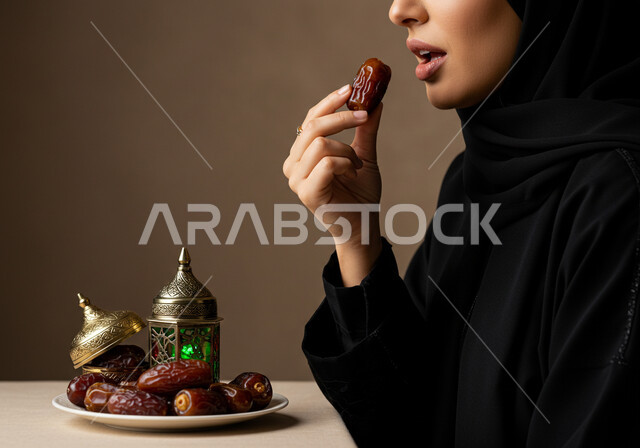 افطار صحي في شهر رمضان المبارك، كسر الصيام بتناول التمر، بورتريه مقرب لإمرأة عربية خليجية سعودية ترتدي الحجاب والعباءة تمسك بيدها حبة رطب شهية، محصول زراعي محلي وطني سعودي، حسن الاستقبال وكرم الضيافة، خلفية بنية