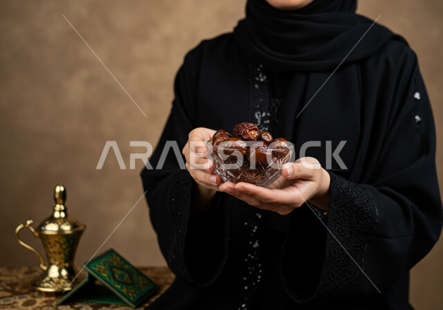 وجبة الرطب الصحية ذات القيمة الغذائية العالية, محصول زراعي محلي وطني سعودي، بورتريه مقرب ليد إمرأة عربية خليجية سعودية ترتدي الحجاب والعباءة تحمل بيدها وعاء مليء بحبات التمر الطازجة, كرم الضيافة وحسن الاستقبال في شهر رمضان المبارك، خلفيه بنية