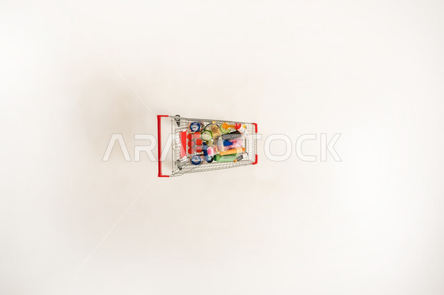 مفهوم التسوق من المراكز التجاريه والسوبرماركت، بورتريه عامودي علوي لعربه تسوق مليئه بالمستلزمات الغذائيه والتموينيه، اختيار اصناف معينه من المأكولات والمشروبات، خلفيه بيضاء