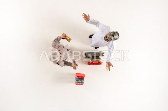 Expressions of confusion in choosing, having a good time shopping, taking advantage of the discount and reduction, vertical overhead portrait of a young Arab Gulf Omani man wearing a dishdasha, a sleeve and sunglasses raising his hands up with gestures of ignorance and lack of knowledge, a veiled woman holding bags in her hand, white background