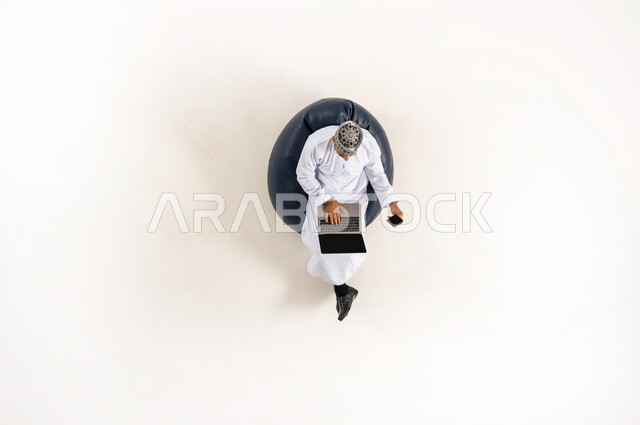 استخدام التكنولوجيا المتطورة والتقنيات الحديثة, بورتريه عامودي علوي لرجل عربي خليجي عماني يرتدي الدشداشة والكمه ويقوم بالدفع الالكتروني بواسطة الحاسوب المحمول, استخدام بطاقة الصراف, سهولة السحب عبر الحساب البنكي, خلفية بيضاء